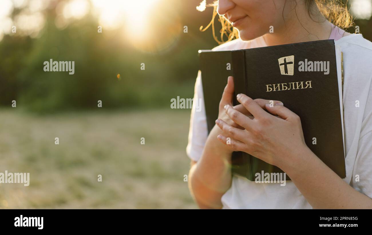 La donna cristiana tiene la bibbia nelle sue mani. Leggere la Sacra Bibbia in un campo durante il bellissimo tramonto. Foto Stock