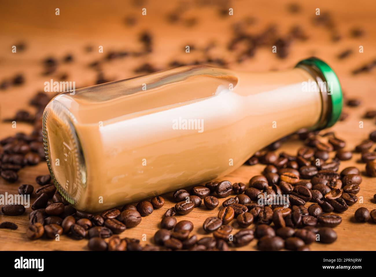 Caffè latte in bottiglia di vetro e caffè in grani sul tavolo di legno. Foto Stock