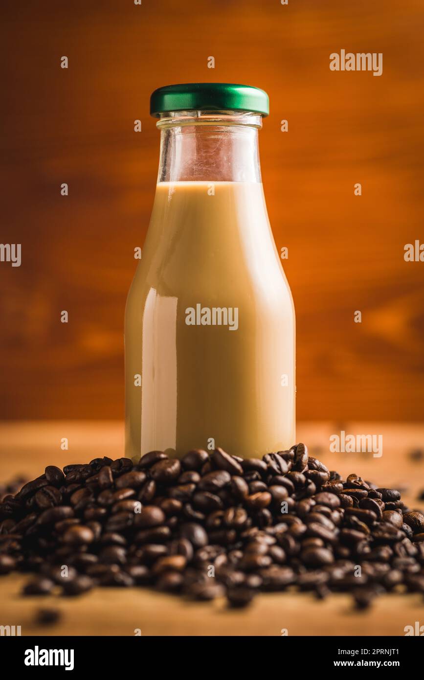 Caffè latte in bottiglia di vetro e caffè in grani sul tavolo di legno. Foto Stock