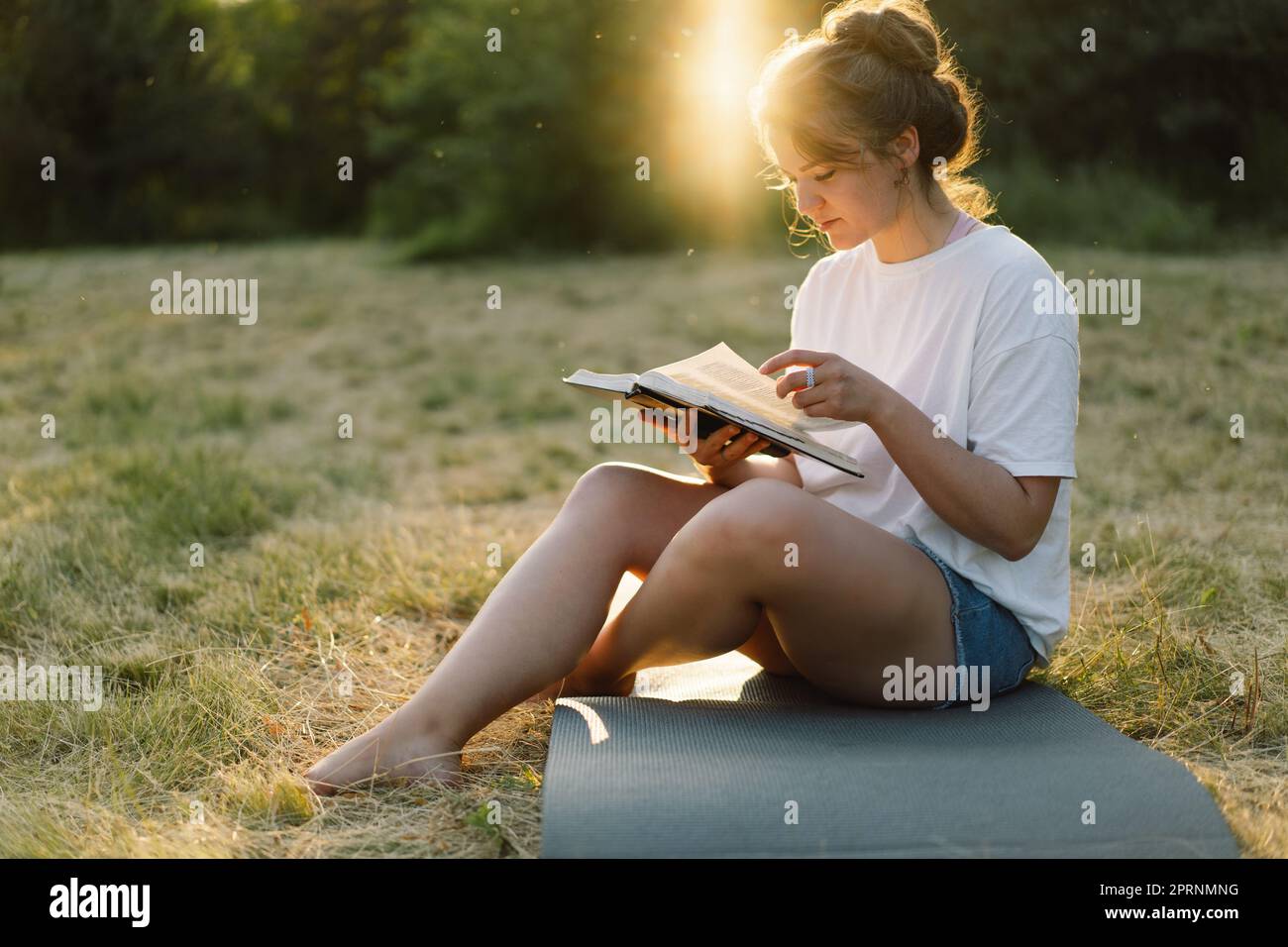 La donna cristiana tiene la bibbia nelle sue mani. Leggere la Sacra Bibbia in un campo durante il bellissimo tramonto. Foto Stock