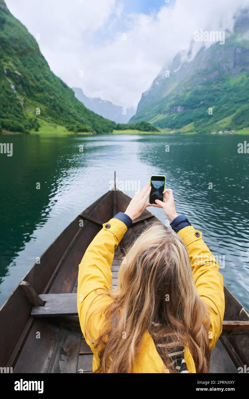 Avventura donna in barca fila scattare foto su smartphone di bellissimo lago fiordo per i social media Foto Stock