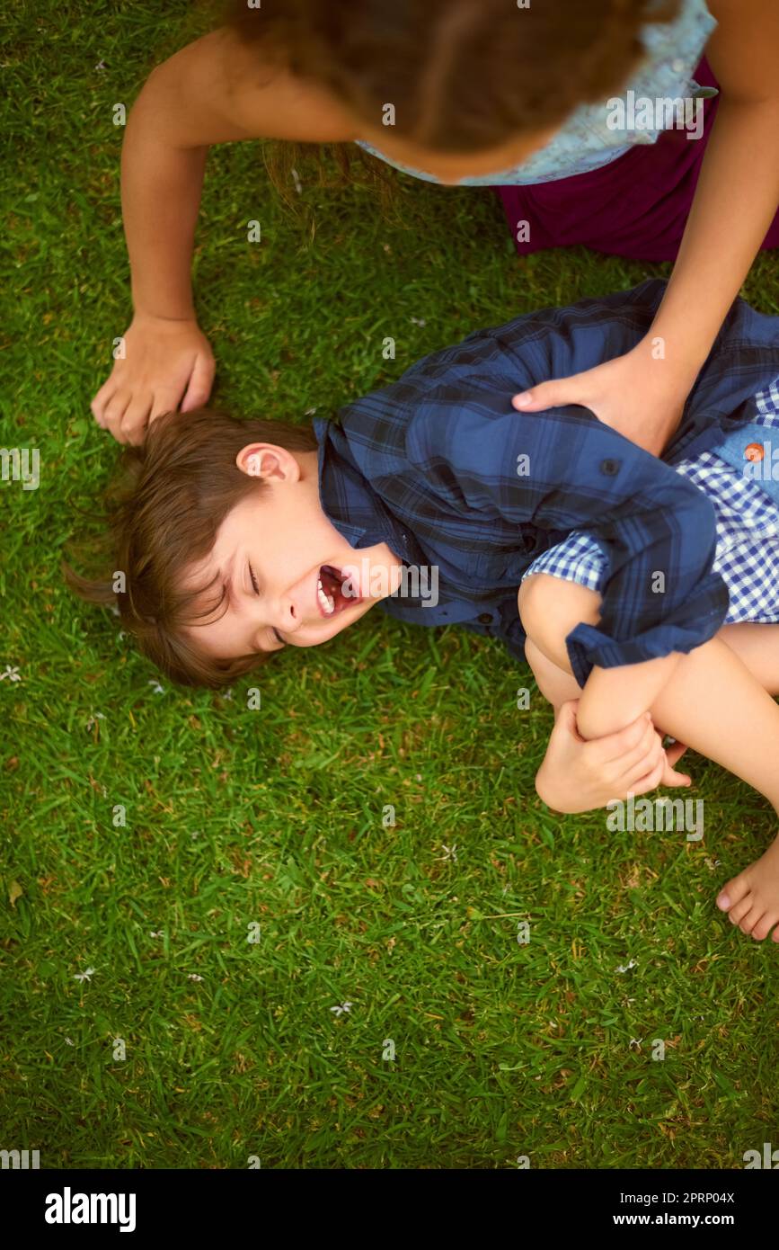 Niente altro che solletico e ridere quando theyre insieme. Colpo ad angolo alto di una giovane ragazza solletico suo fratello mentre gioca fuori sul prato. Foto Stock