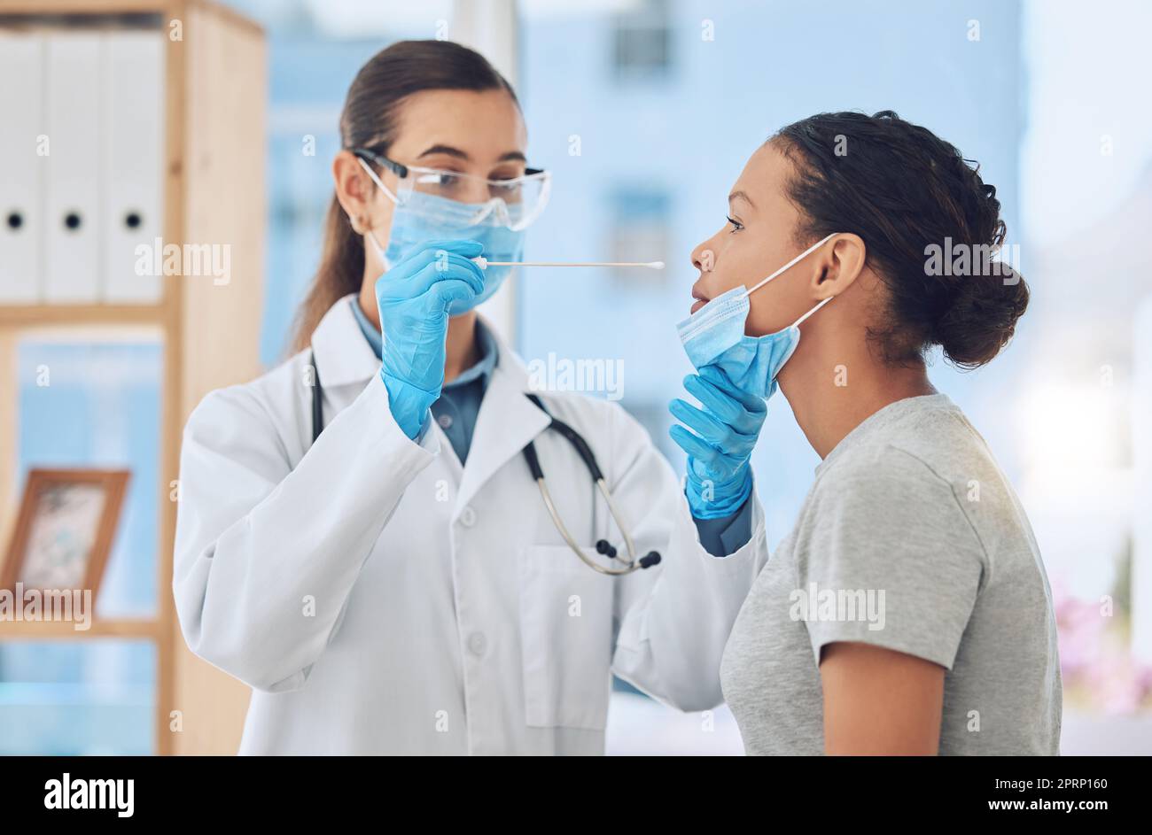 Medico che fa un test covid su una paziente prelevando un campione con tampone naso nel suo ufficio. Operatore sanitario e donna con maschera facciale in consultazione clinica durante la pandemia di coronavirus in ospedale Foto Stock