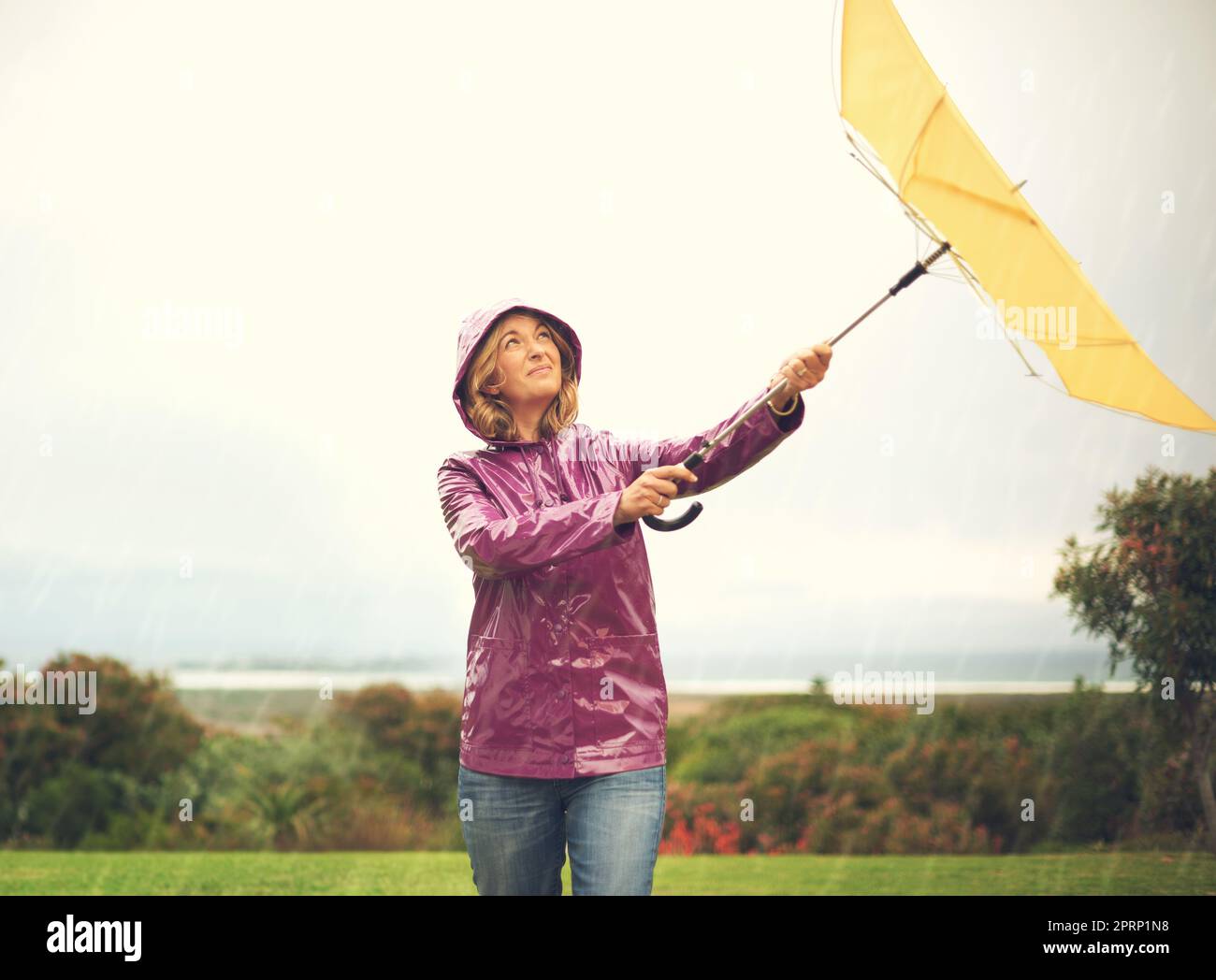 Un po' di cielo limpido potrebbe essere d'aiuto: Una donna che si trova fuori sotto la pioggia e che tiene un ombrello che guarda in alto nel cielo. Foto Stock