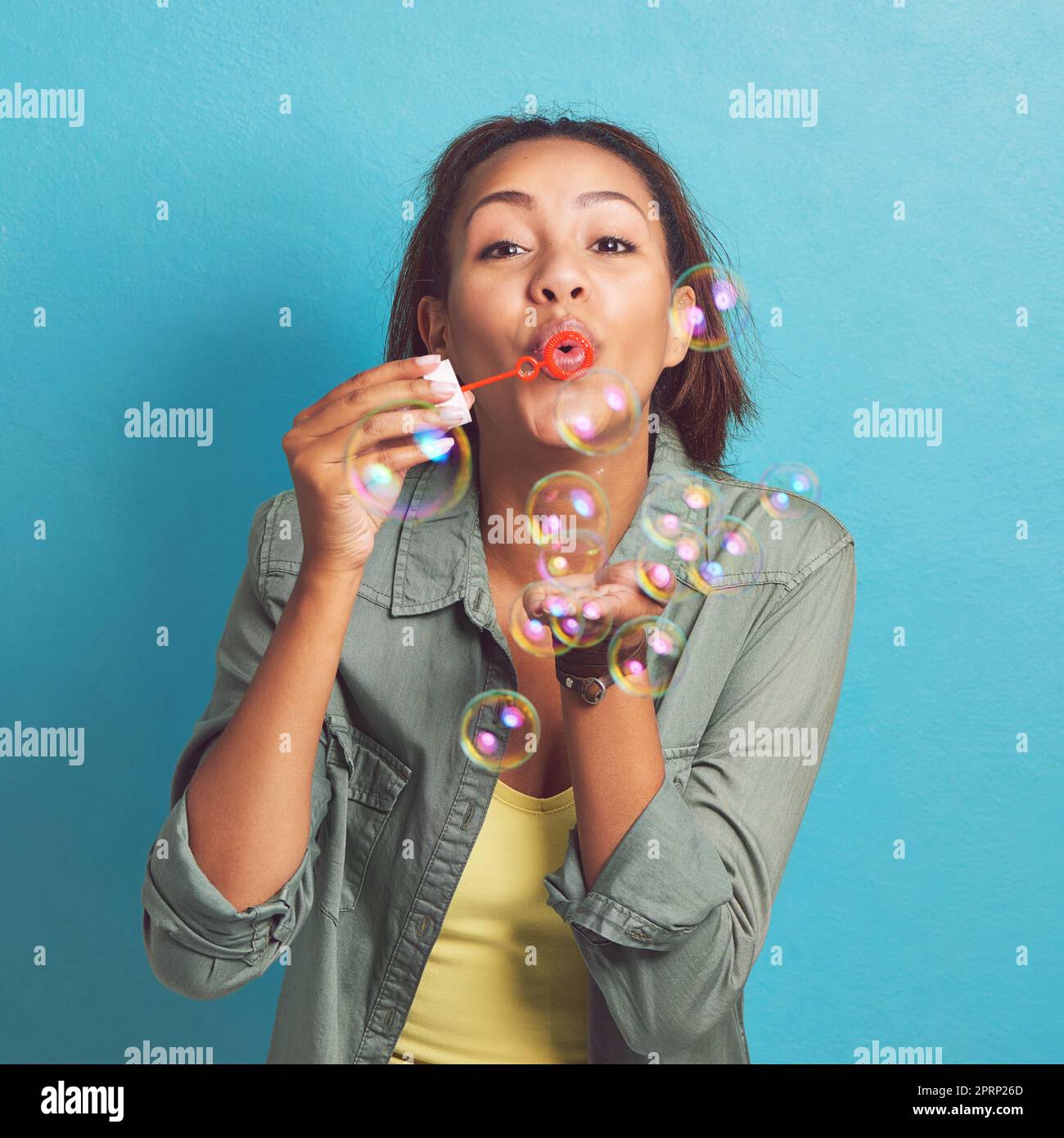 Che tutti i vostri problemi siano bolle. Ritratto di una giovane donna che soffia bolle su sfondo blu. Foto Stock