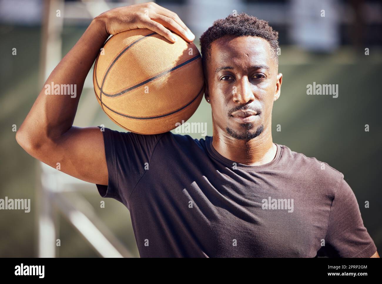 Ritratto un uomo afro-americano in piedi con un pallacanestro in campo. Atleta maschile o giocatore che tiene una palla sportiva dopo aver giocato, allenato e praticato un gioco in background su un campo Foto Stock