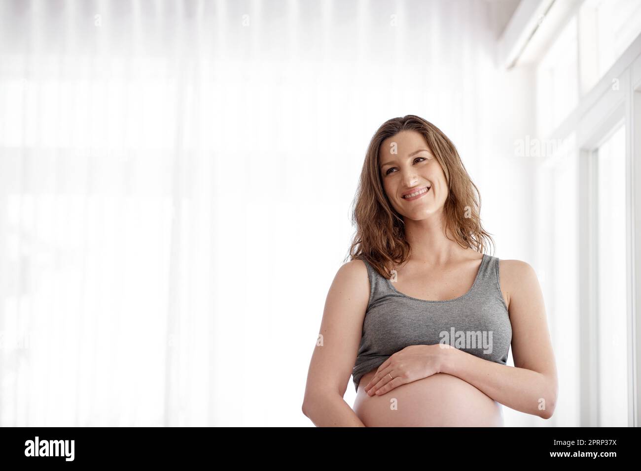Anticipando l'arrivo del suo bambino. Una giovane donna incinta in piedi nella sua casa. Foto Stock