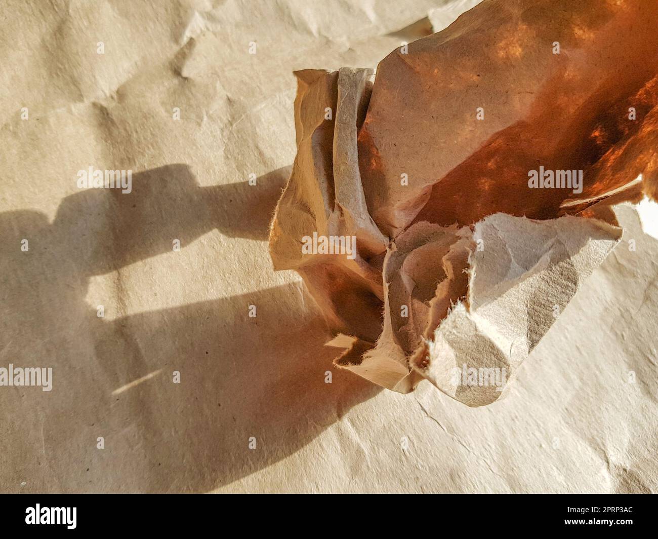 Un foglio accartocciato di carta artigianale in una palla sullo sfondo, vista dall'alto, luce solare brillante e ombra. Foto Stock