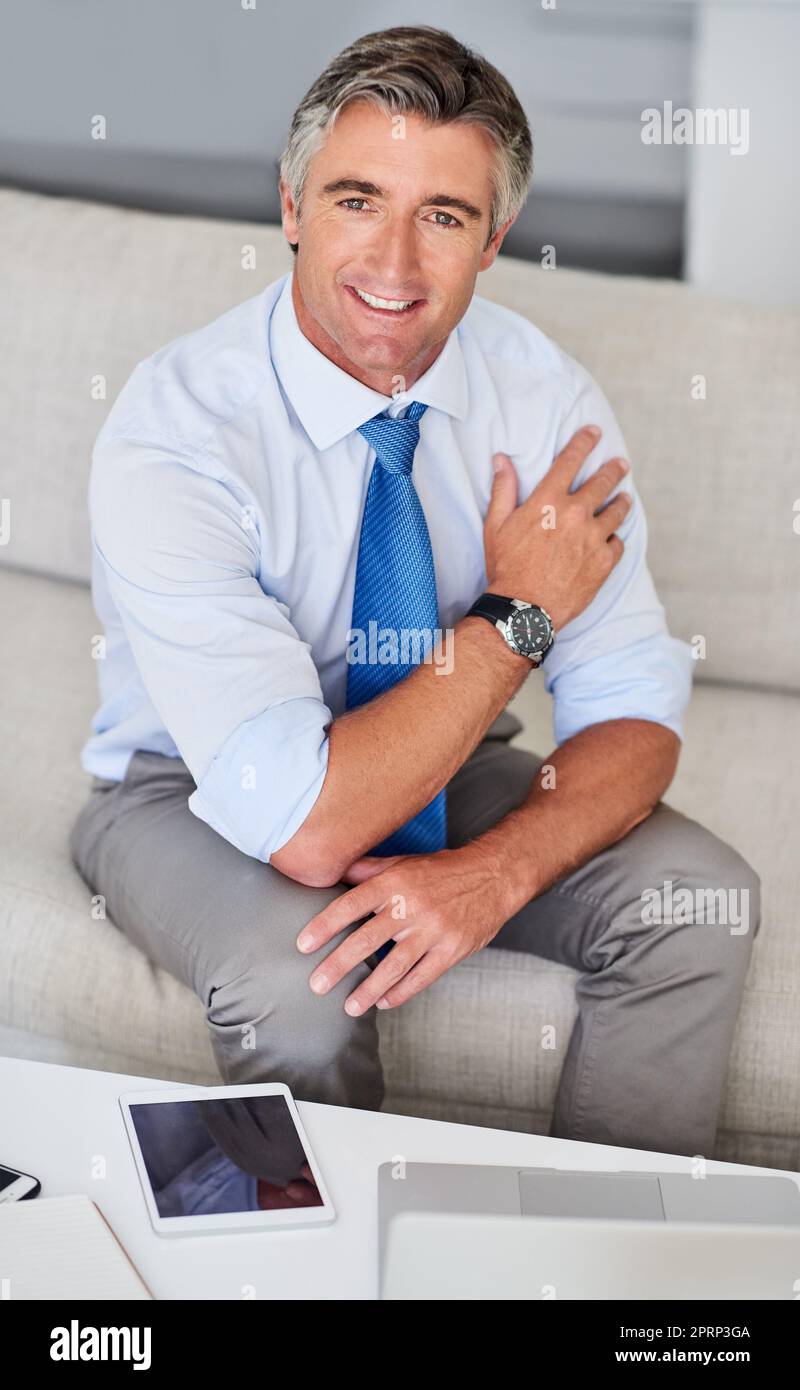 La fiducia genera il successo. Ritratto di un uomo d'affari maturo che indossa una tuta e sorride mentre si siede su un divano all'interno. Foto Stock