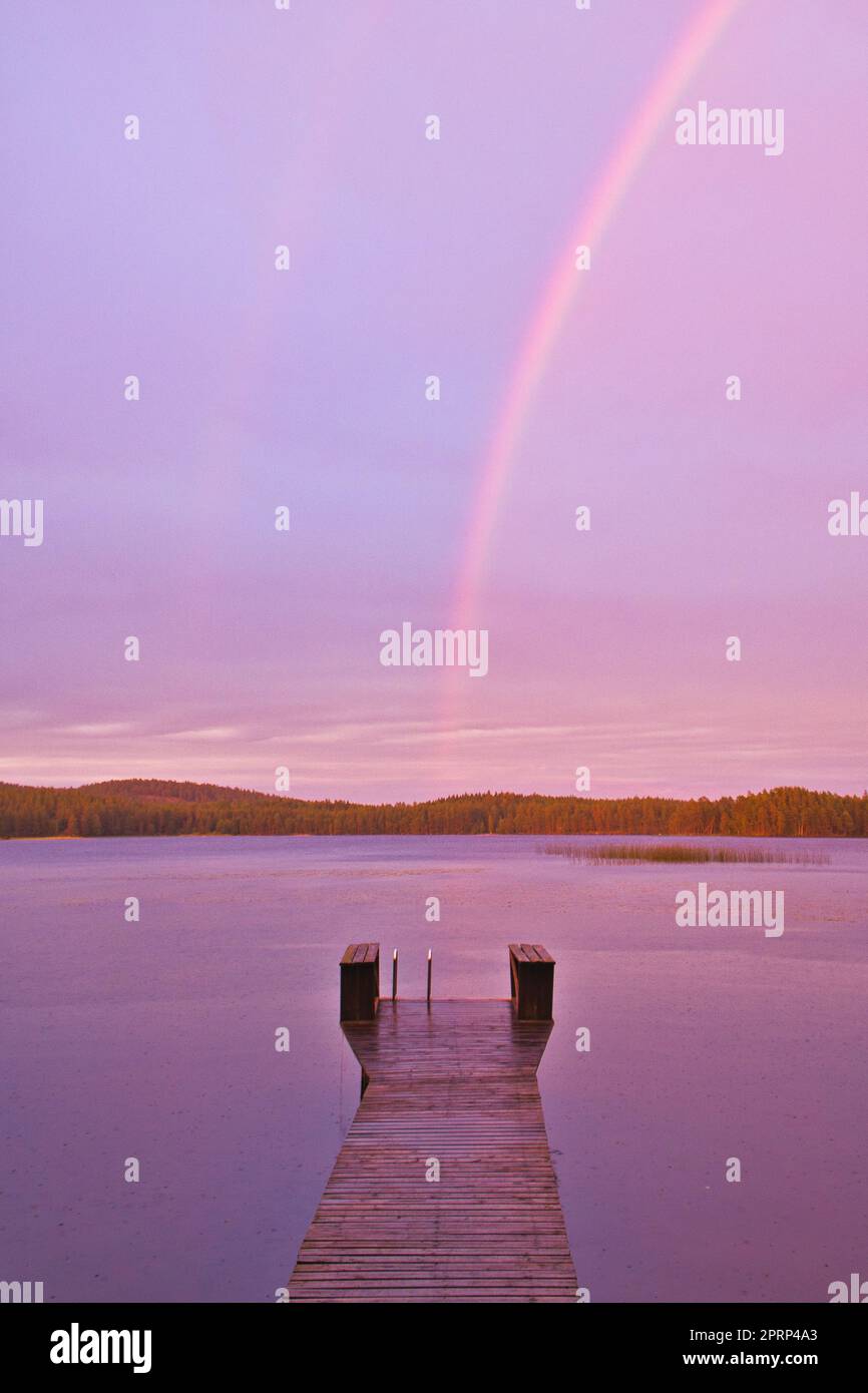 Passerella che raggiunge l'acqua al tramonto con l'arcobaleno sullo sfondo quando piove Foto Stock