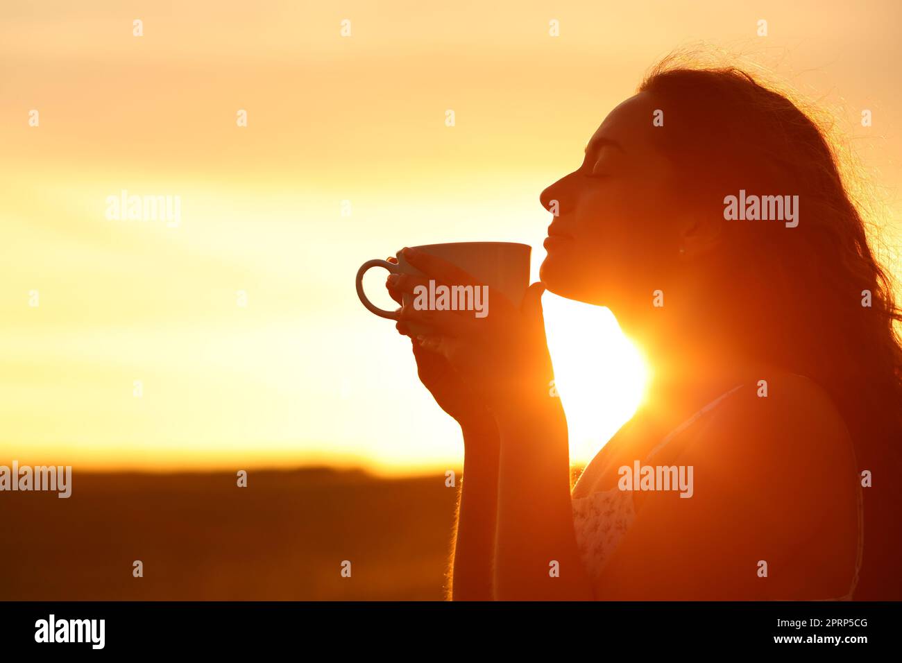 Silhouette di una donna che puzza di caffè al tramonto Foto Stock