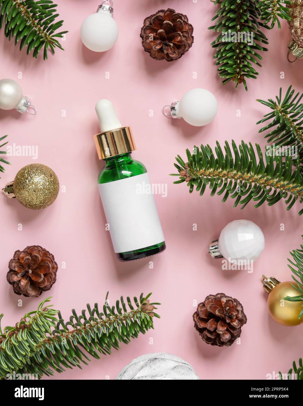 Flacone cosmetico con contagocce vicino alle decorazioni natalizie, rami di abete e coni di pino rosa, mockup Foto Stock