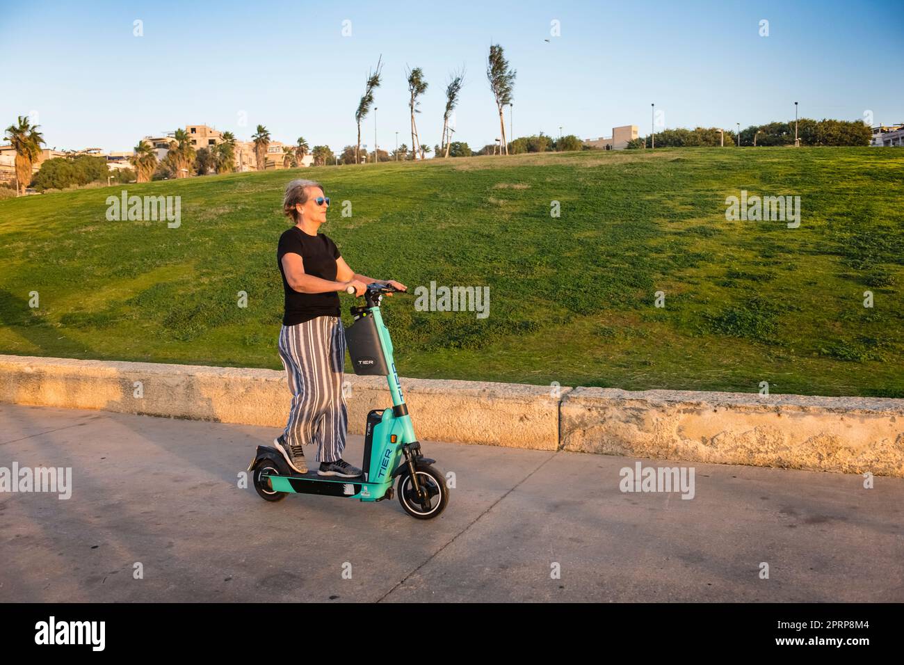 Giovane attivo a cuore 60s Lady/Woman utilizzando scooter elettrico sul lungomare a Tel Aviv Israele Foto Stock