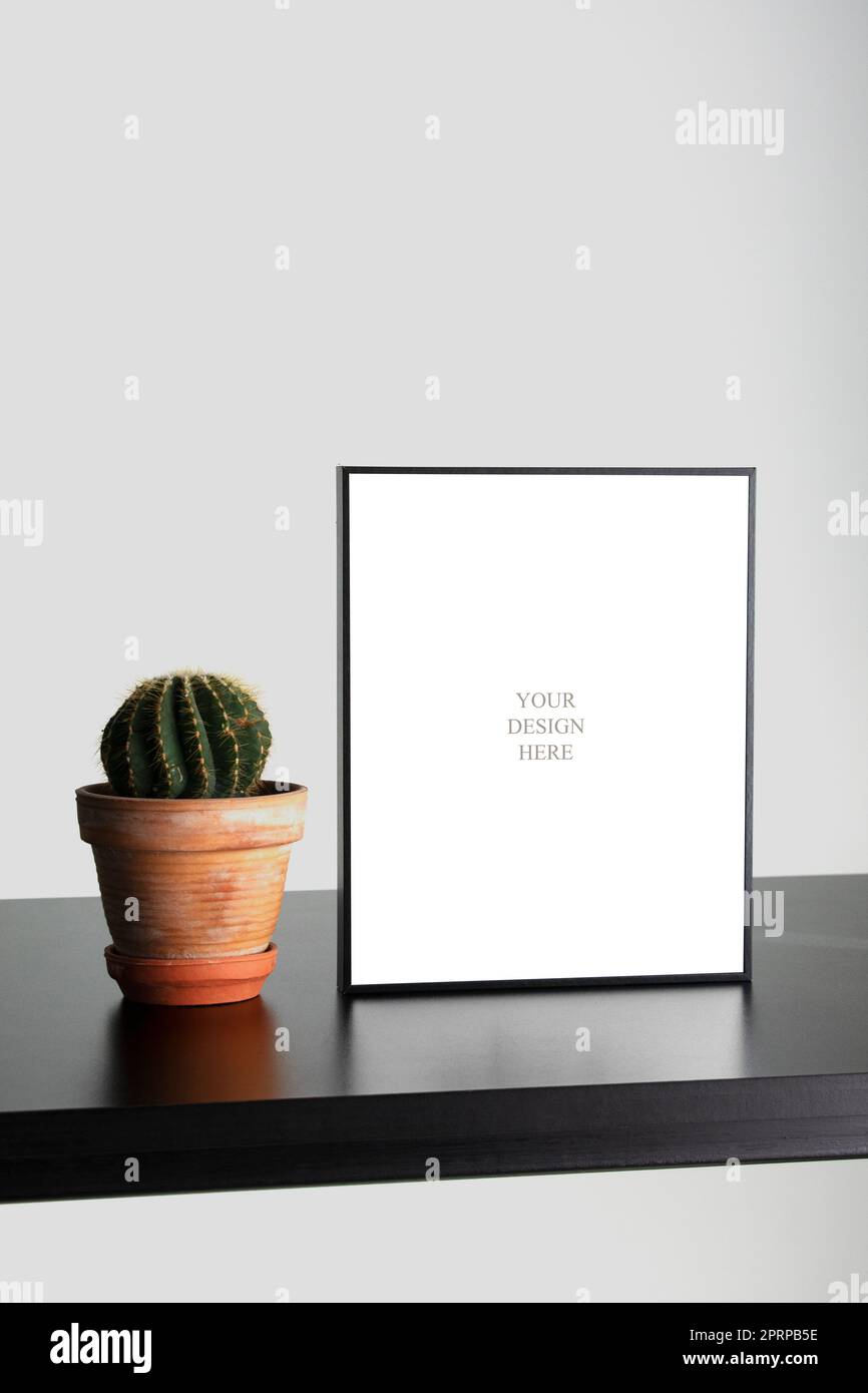 Mockup - cornice fotografica nera sulla scrivania di legno nero con parete succulenta e bianca in studio ufficio Foto Stock