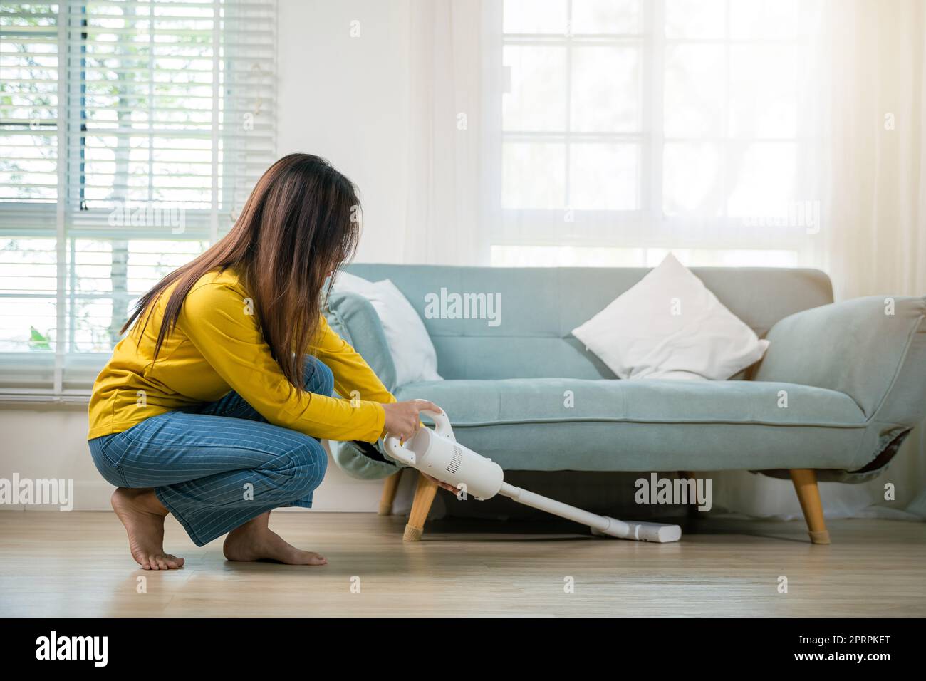 Casalinga donna polvere pulizia pavimento sotto divano o divano mobili con aspirapolvere Foto Stock