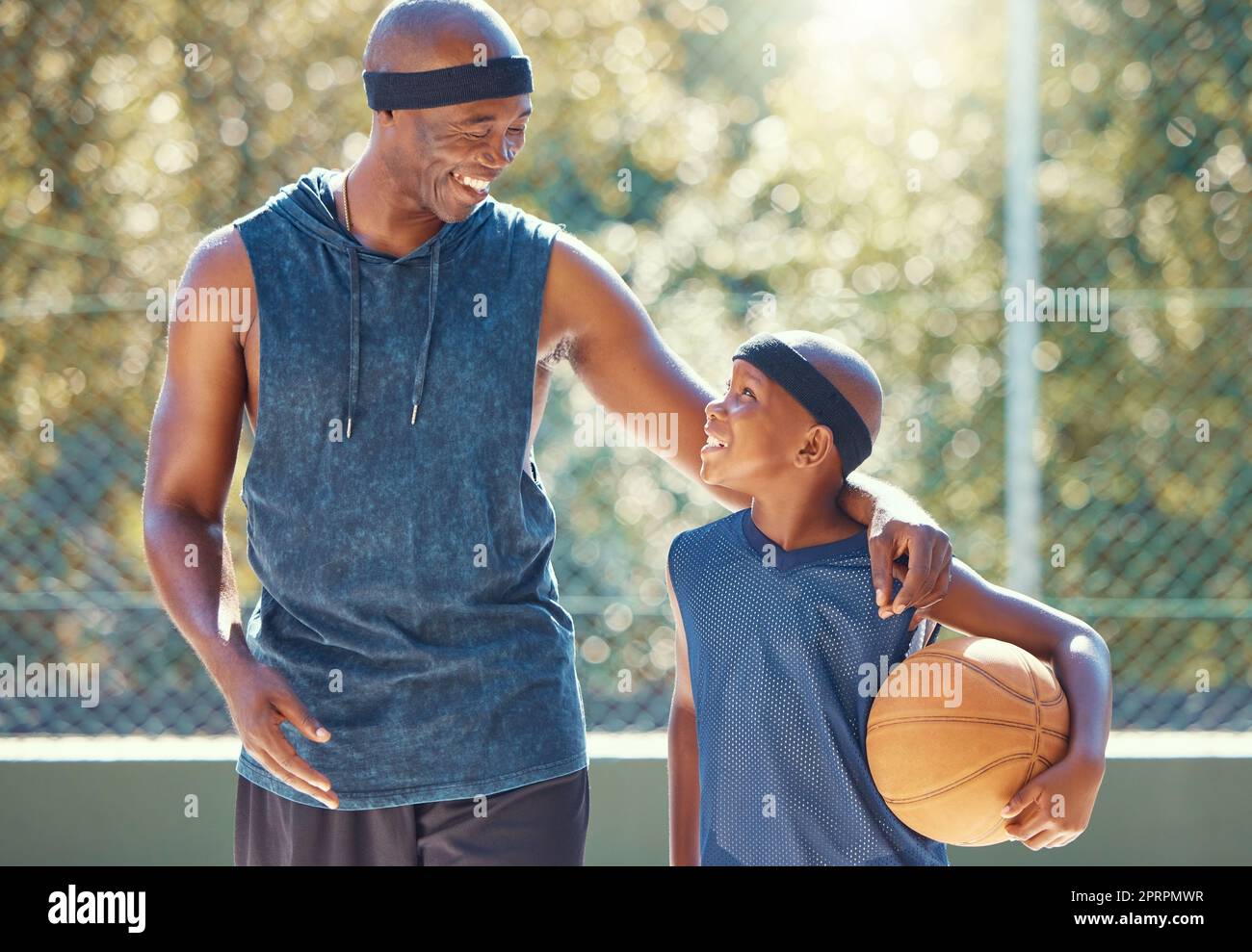 Padre felice, figlio e pallacanestro di neri pronti per una partita, insegnare e imparare in un campo. Uomo e ragazzo africani in esercizio di motivazione sportiva, allenamento e allenamento sorridendo insieme nella natura Foto Stock