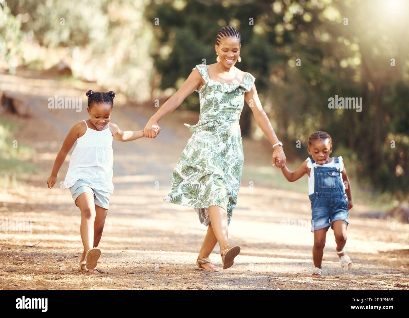 Felice, madre e bambini che camminano in una foresta tenendosi per mano nella natura in allegria e sorridendo. Famiglia nera di una mamma e delle sue bambine che si uniscono in una divertente passeggiata nell'ambiente naturale all'aperto Foto Stock