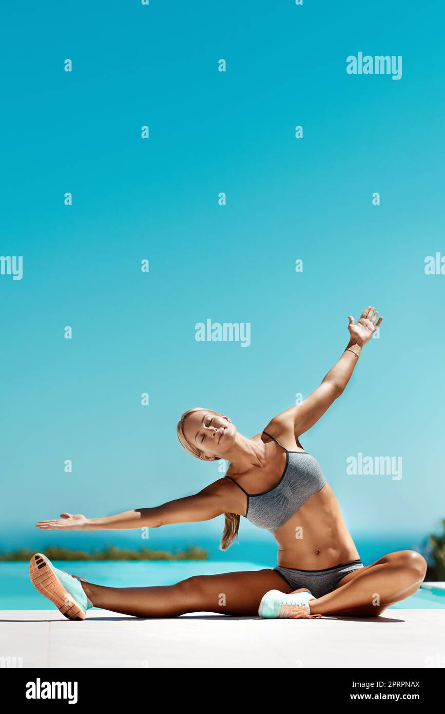 Respira attraverso il stretching. Una giovane donna attraente e in forma che si allunga con le braccia distese dalla piscina dopo il suo allenamento. Foto Stock