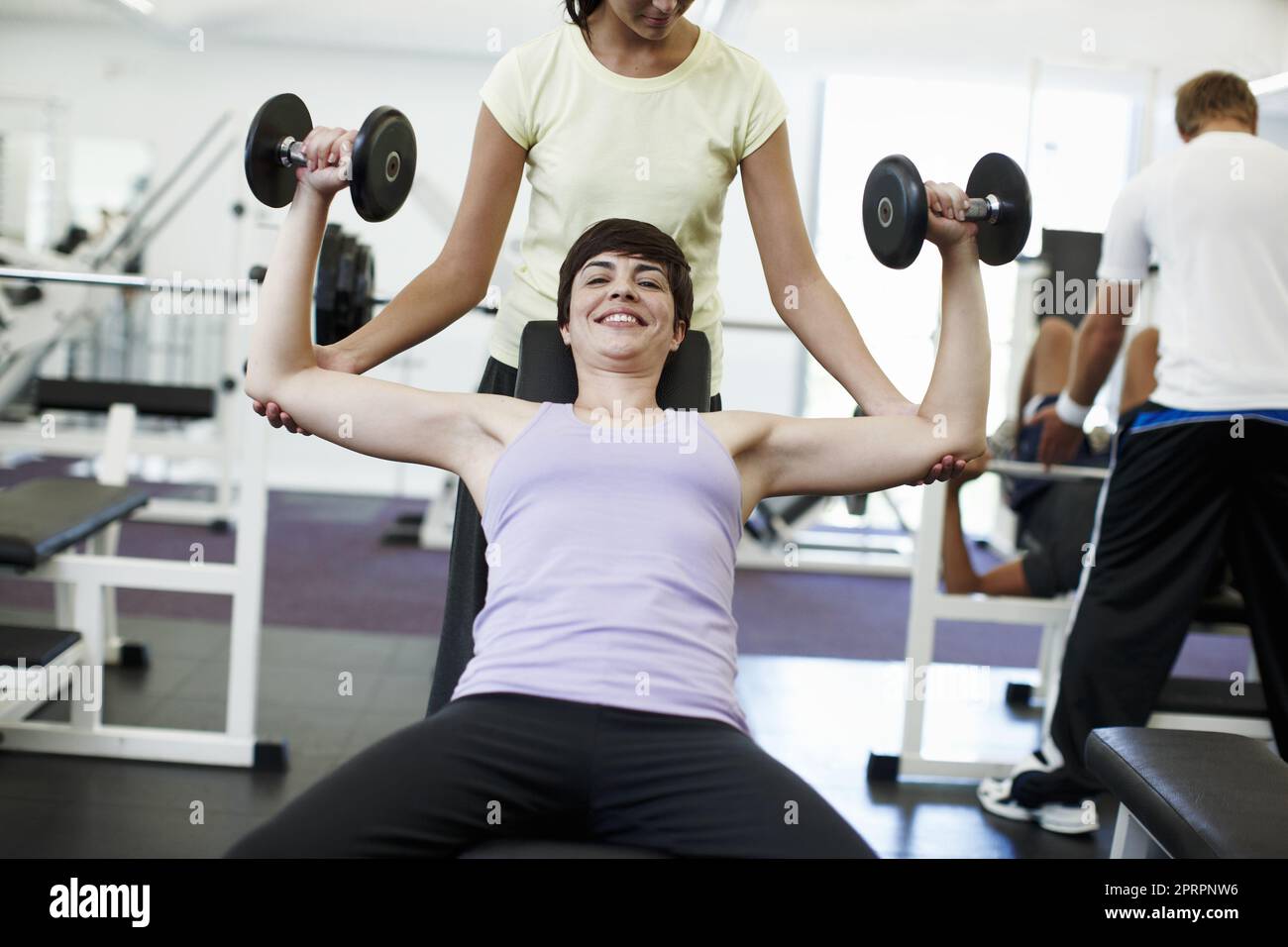 Offre un grande aiuto. Una giovane donna attraente allenarsi sui pesi con il suo personal trainer. Foto Stock