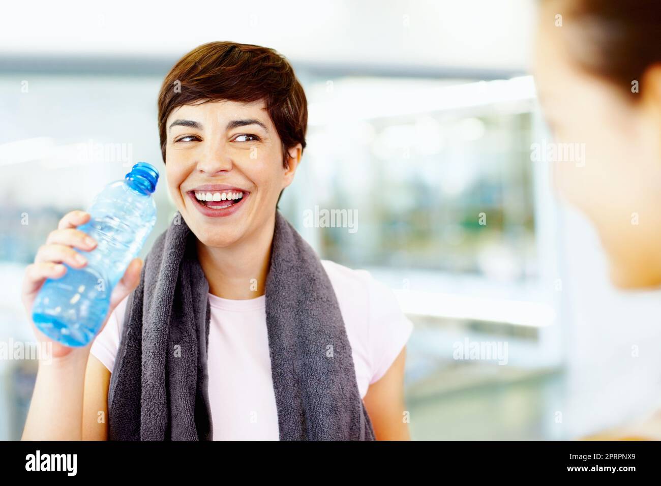 Femmine rinfrescanti dopo l'allenamento in palestra. Donna beve acqua mentre chiacchiera con gli amici al centro fitness. Foto Stock