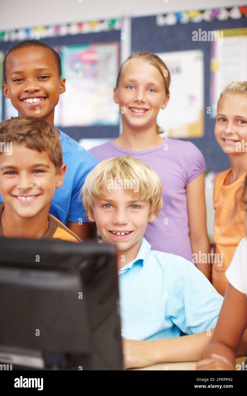 Abbiamo un sacco di tempo libero sui computer. Ritratto di un giovane gruppo di bambini seduti e in piedi attorno al computer durante la lezione. Foto Stock