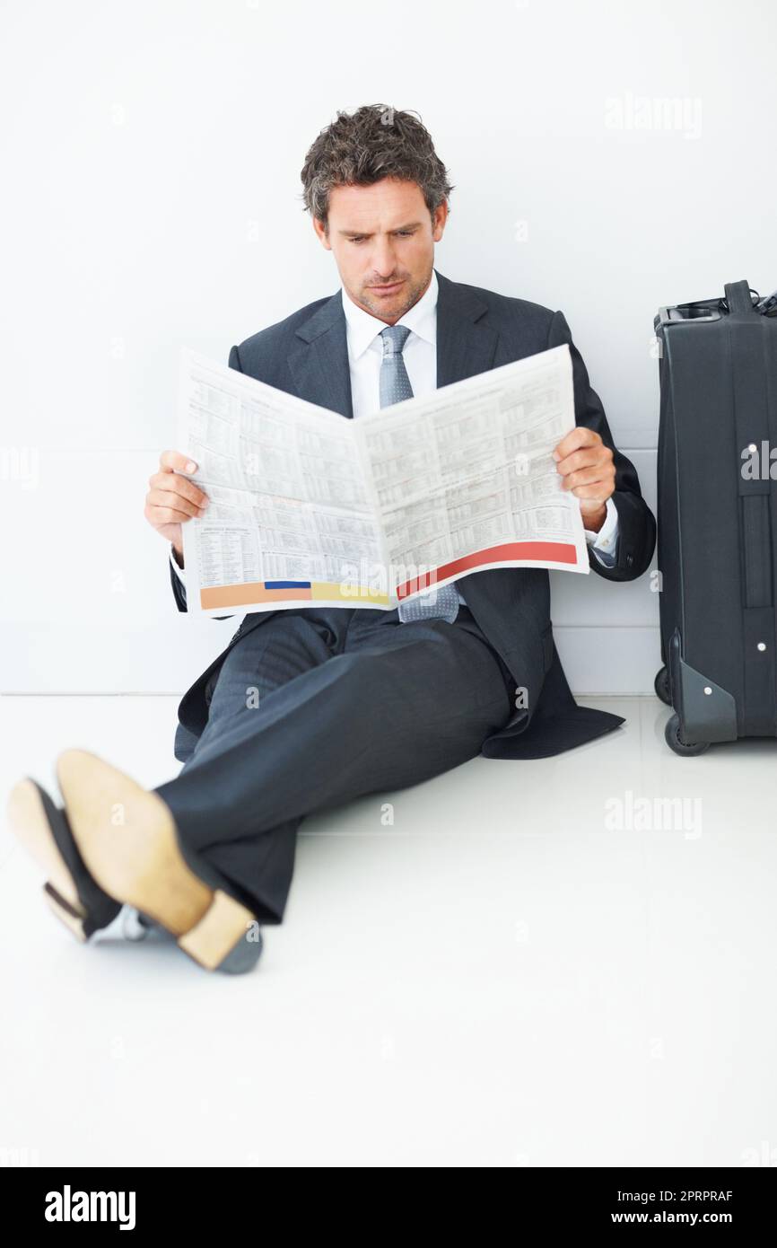 Uomo d'affari di media età che legge il giornale. Uomo d'affari di mezza età con bagagli da viaggio seduti contro le pareti e leggendo il giornale. Foto Stock