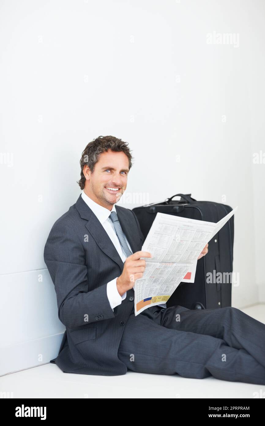 Uomo d'affari sorridente e leggendo un giornale. Uomo d'affari sorridente astuto che siede contro la parete che legge il giornale e che vi dà un sorriso caldo. Foto Stock