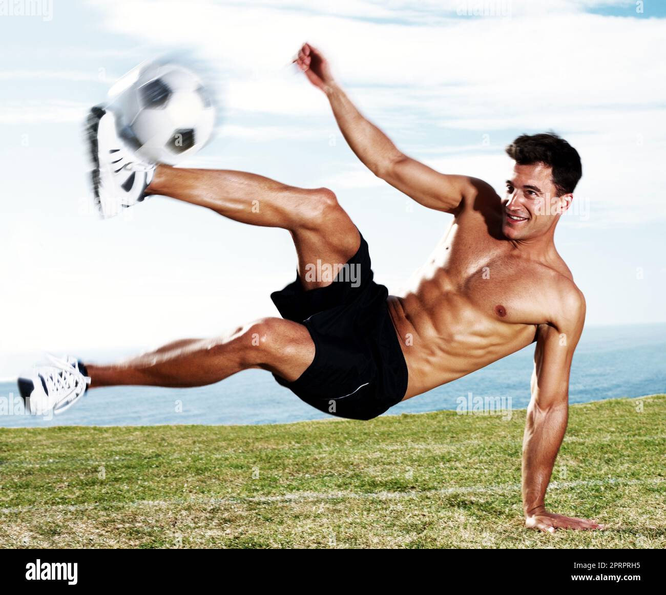 Giovane giocatore di calcio che calcia il calcio in azione. Ritratto di un giovane giocatore di calcio che calcia il calcio in azione contro il cielo. Foto Stock