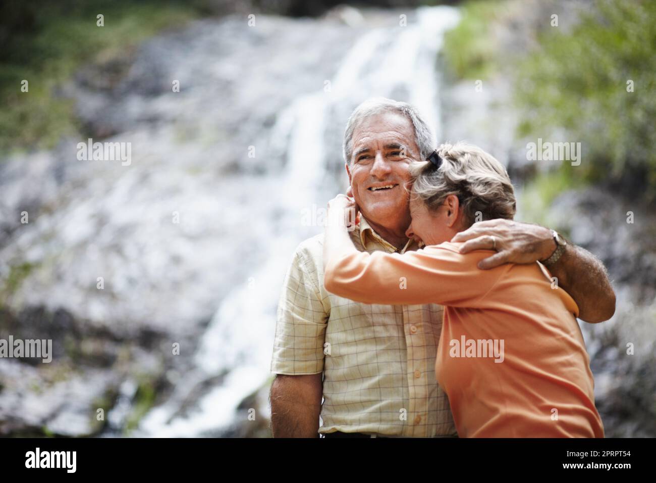 Condividere momenti meravigliosi insieme. Un'affettuosa coppia anziana che si erge sullo sfondo di una pittoresca cascata. Foto Stock