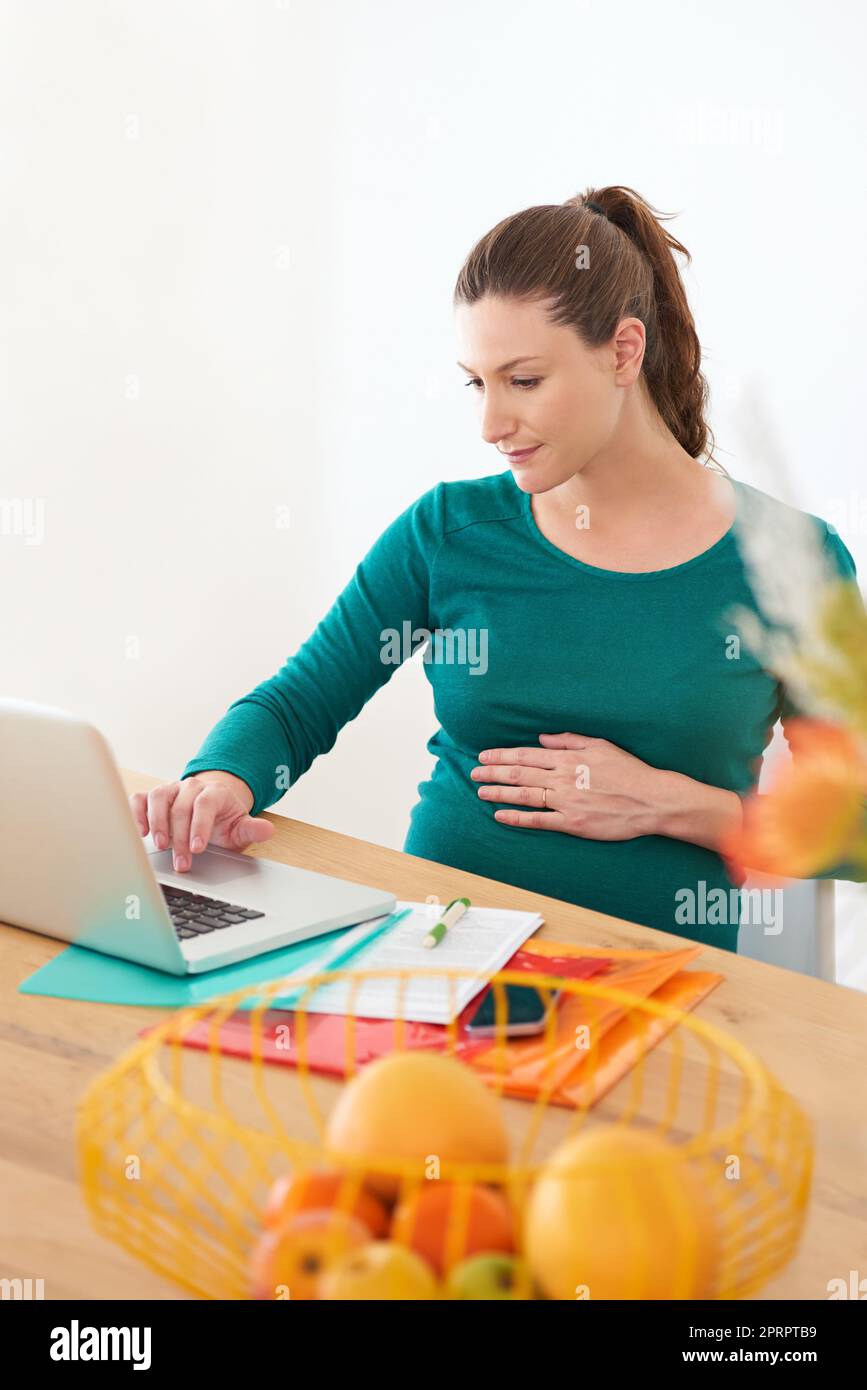 Preparandosi per l'arrivo del suo bambino con la ricerca in linea. Una donna incinta che usa il suo laptop a casa. Foto Stock