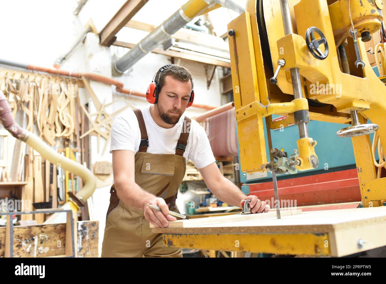 Ritratto di un falegname in abiti da lavoro e di protezione dell'udito in officina di una bottega del falegname Foto Stock