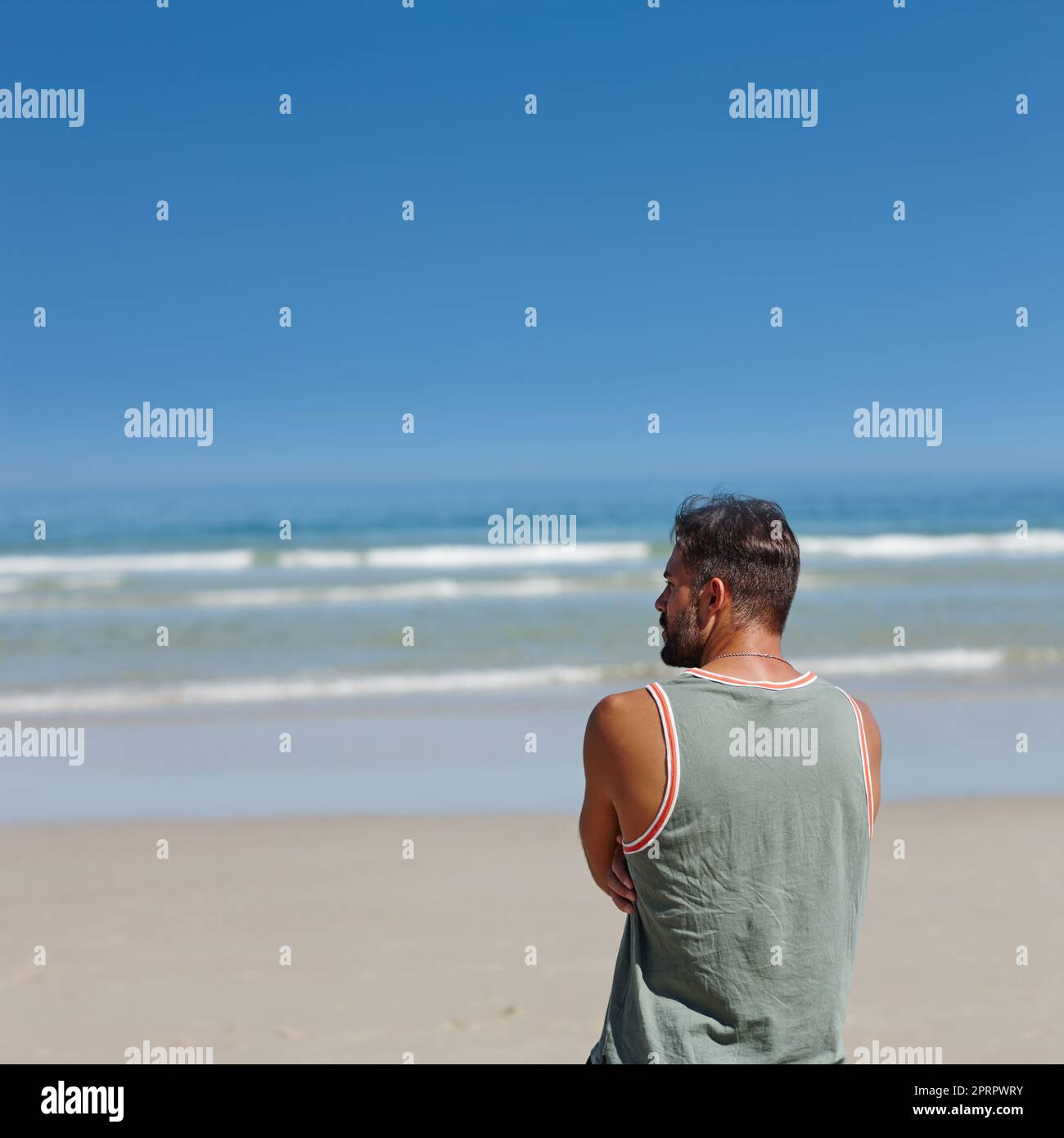 Solitudine sabbiosa. Ripresa da dietro di un giovane uomo che guarda l'oceano. Foto Stock