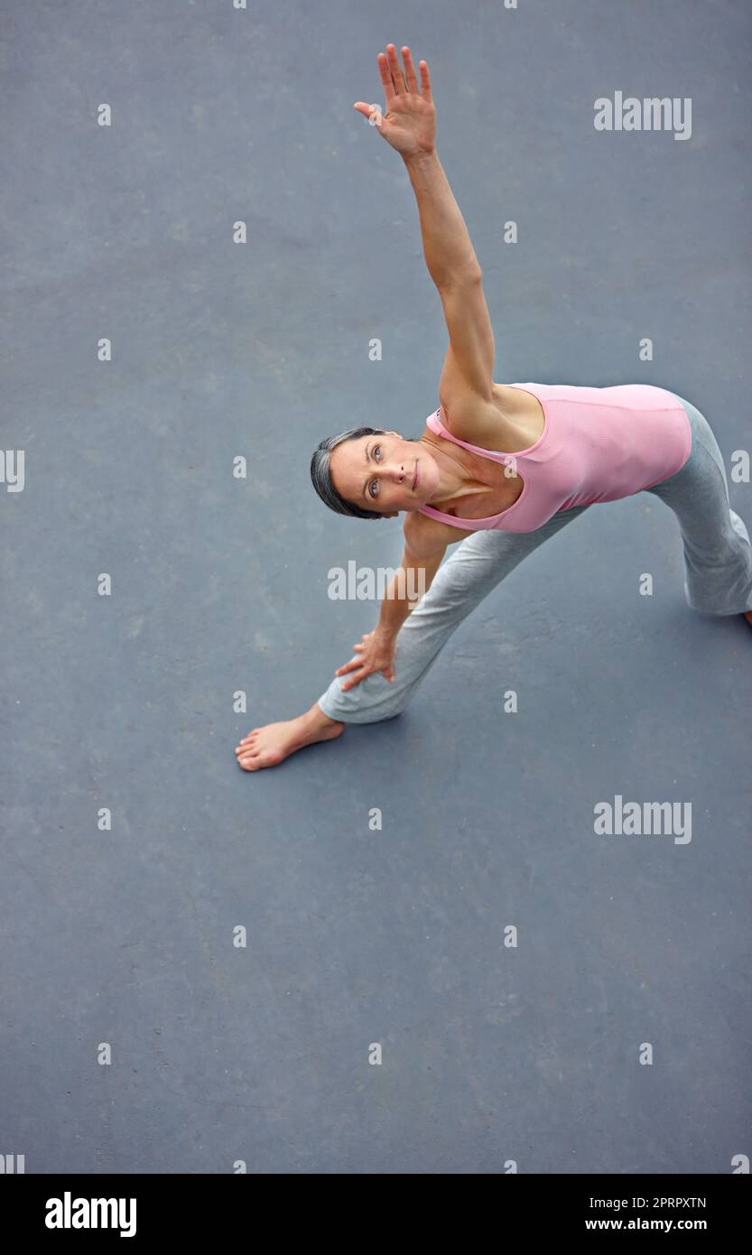 Perfezionare la posa del triangolo. Una donna matura che fa la posa estesa di yoga del triangolo all'aperto. Foto Stock
