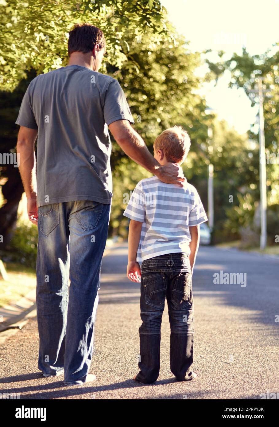 Passeggiando in periferia. Ripresa da dietro di un padre e un figlio che camminano per la strada insieme. Foto Stock
