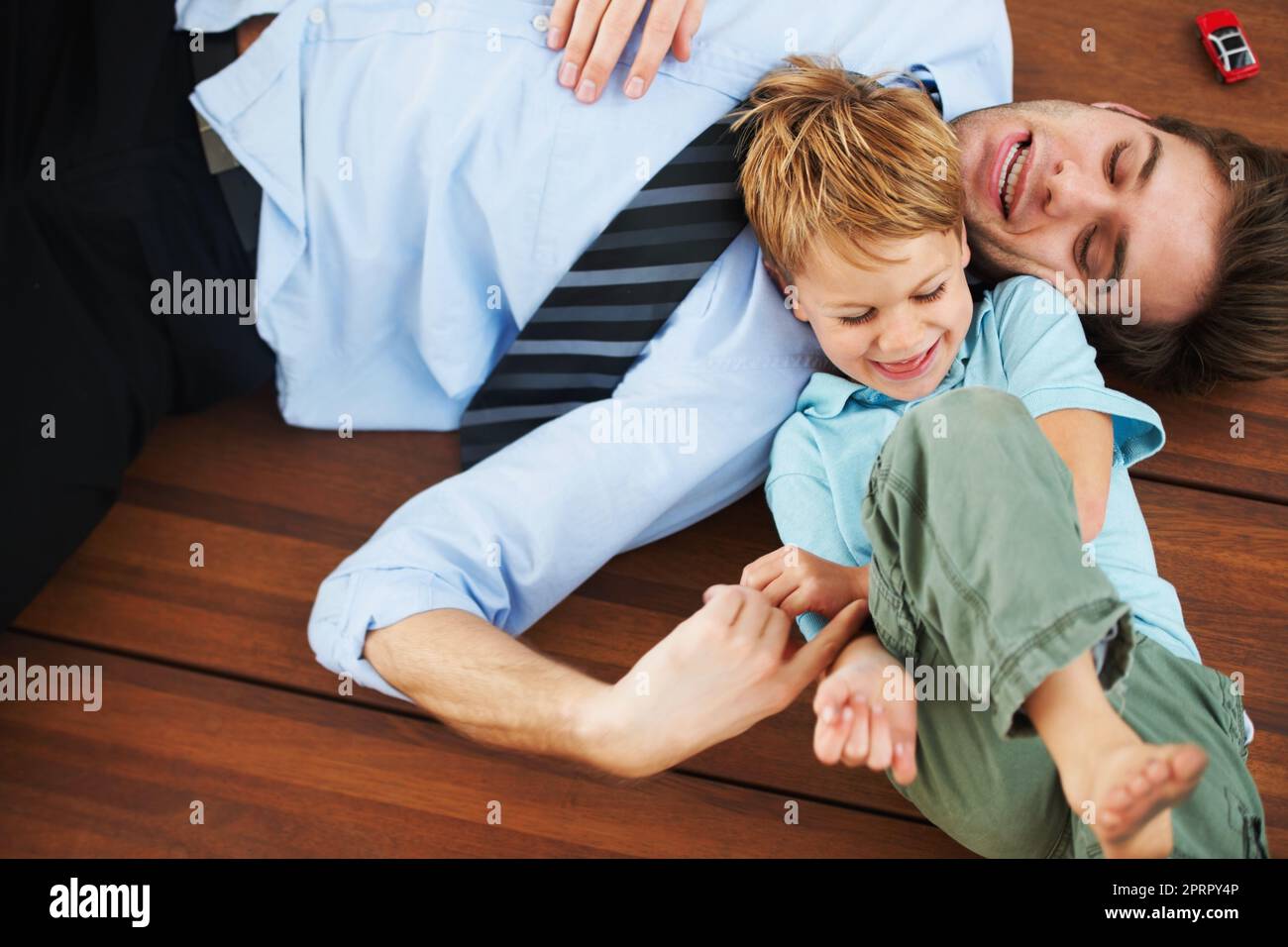 Basta papà, che solletico. Un ragazzino carino che ride sul pavimento mentre è solletico dal suo giovane padre. Foto Stock