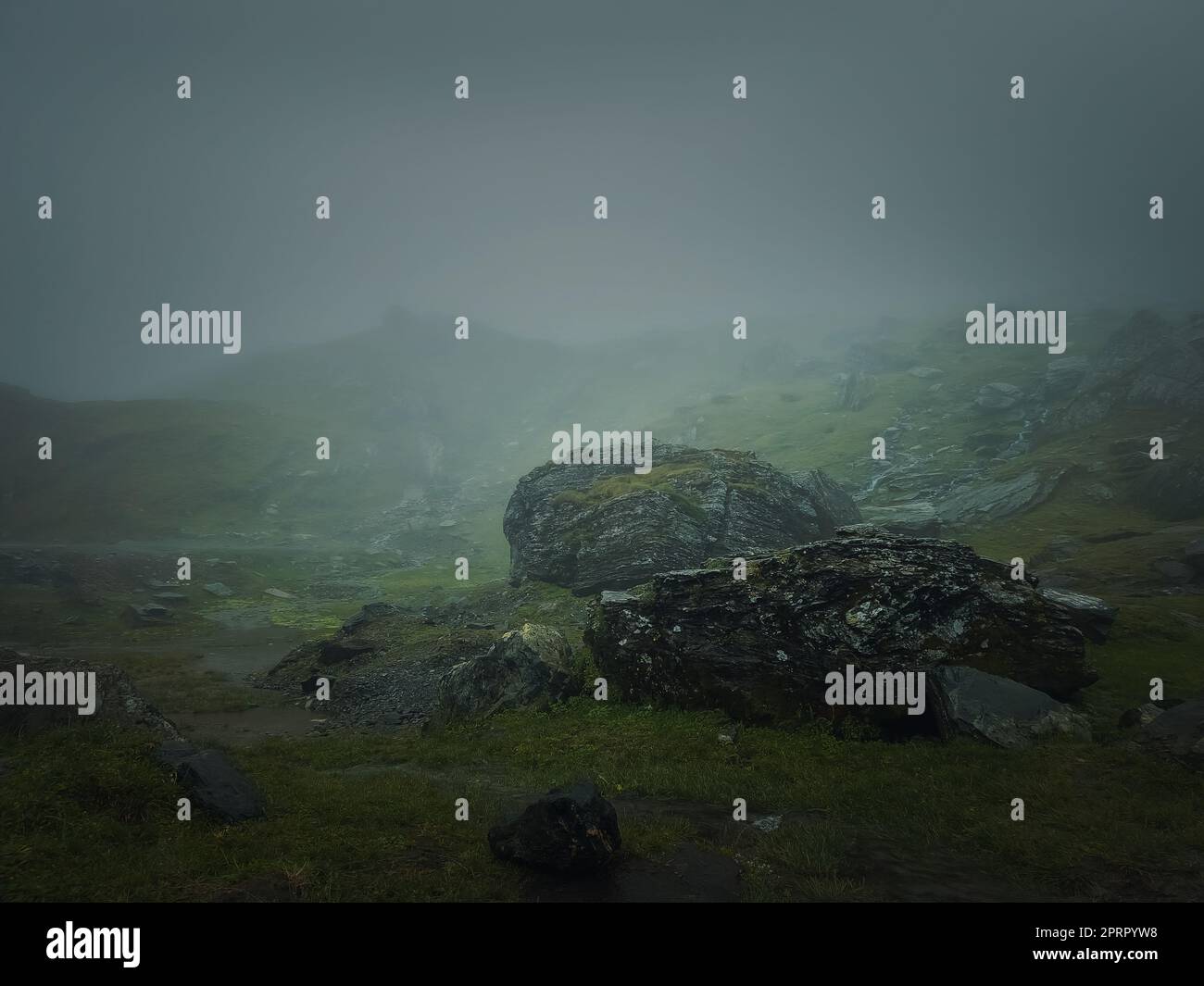 Grandi rocce di montagna e massi visti attraverso la fitta nebbia. Moody scenario escursionistico con tempo piovoso Foto Stock
