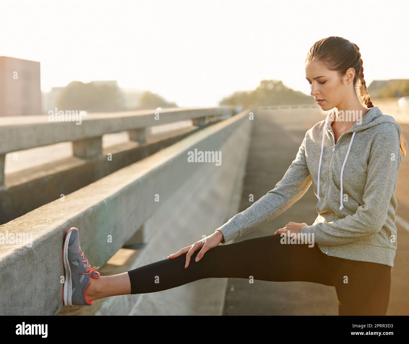 Stay limber and focused. Un giovane jogger femminile che si allunga sulla strada prima di una corsa. Foto Stock