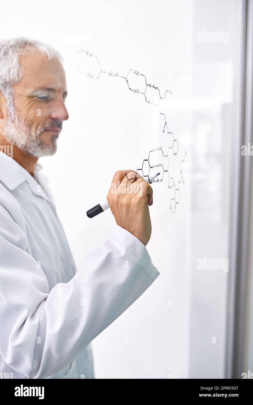 Genius al lavoro. Uno scienziato maschio maturo che attinge legami chimici su una superficie di vetro. Foto Stock