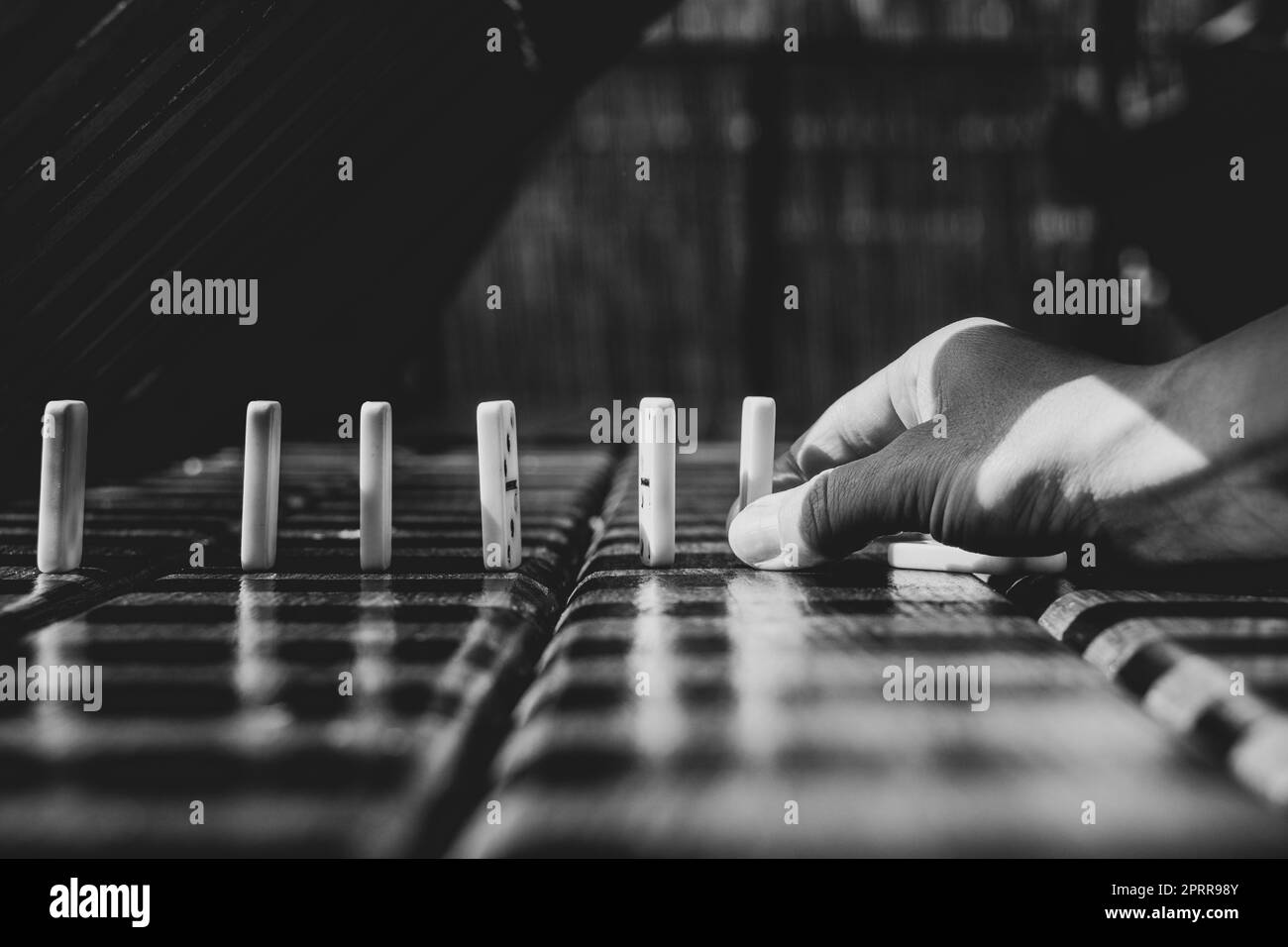 Mano femminile e domino su un tavolo di legno, foto in bianco e nero Foto Stock