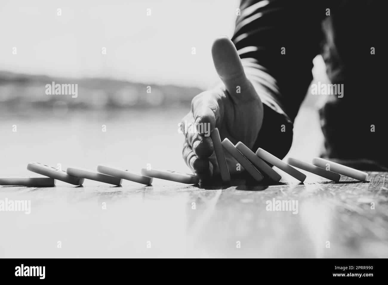 Mano femminile e domino su un tavolo di legno, foto in bianco e nero Foto Stock
