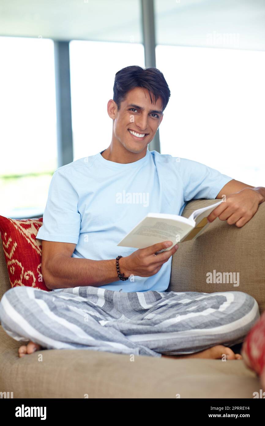 Dormi di meno, legga di più. Un bel giovane seduto sul suo divano mentre legge un libro. Foto Stock