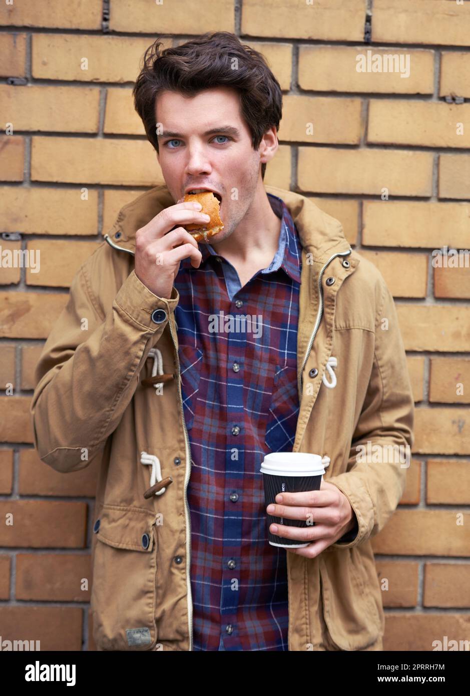 Questo è ciò che io definisco una cena raffinata: Un giovane all'aperto con un hamburger e un caffè da portare via a metà. Foto Stock