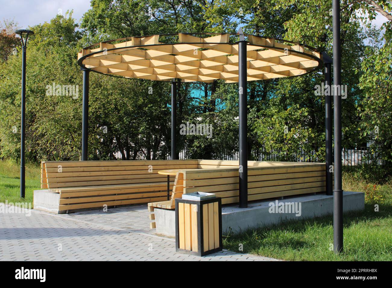 Un gazebo di legno chiaro con una panca, un tavolo e un insolito hutch in un parco cittadino. Architettura urbana Foto Stock