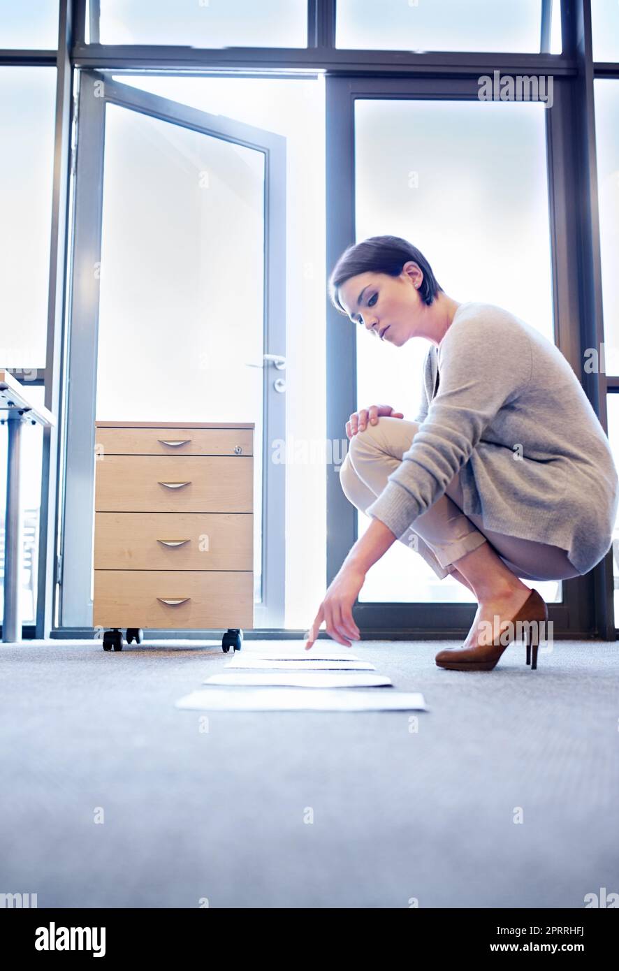 Avere una visione diversa a volte aiuta. Una giovane donna attraente che guarda le carte allineate sul pavimento. Foto Stock