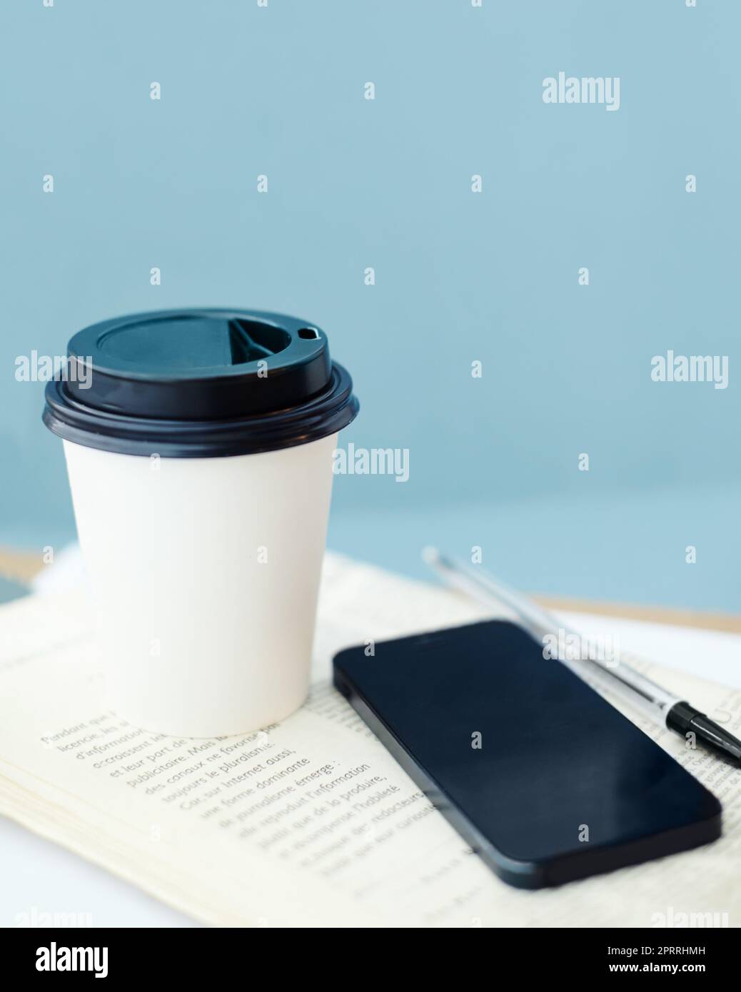 Pausa caffè veloce. Una tazza da caffè usa e getta che si trova sopra un giornale, con una penna e uno smartphone. Foto Stock