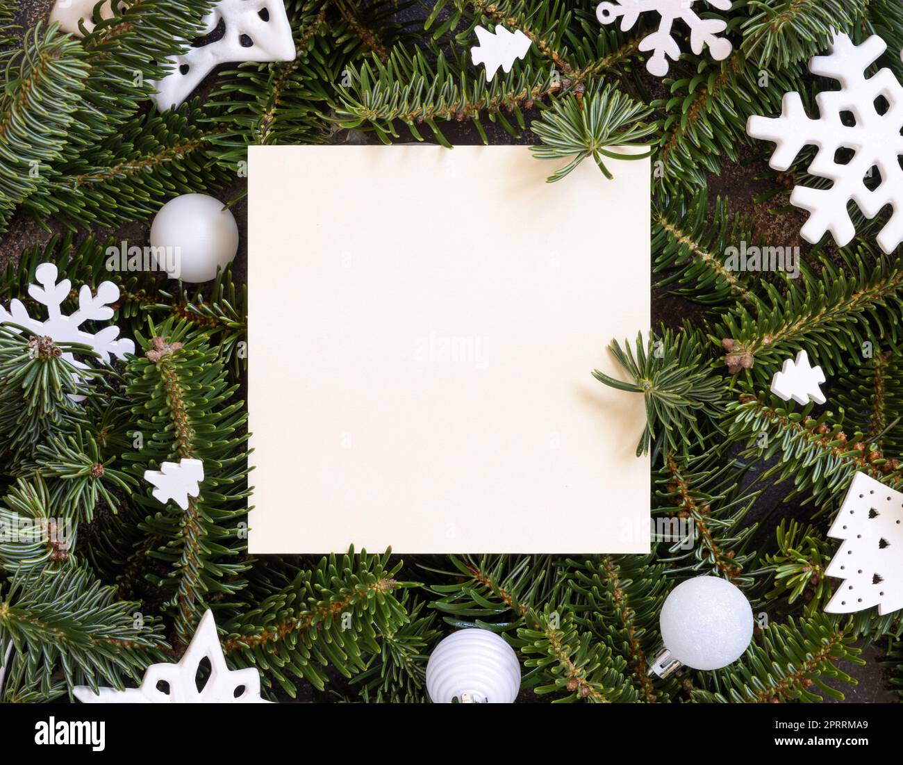 Cartolina quadrata tra decorazioni natalizie bianche e rami di abete verde Foto Stock