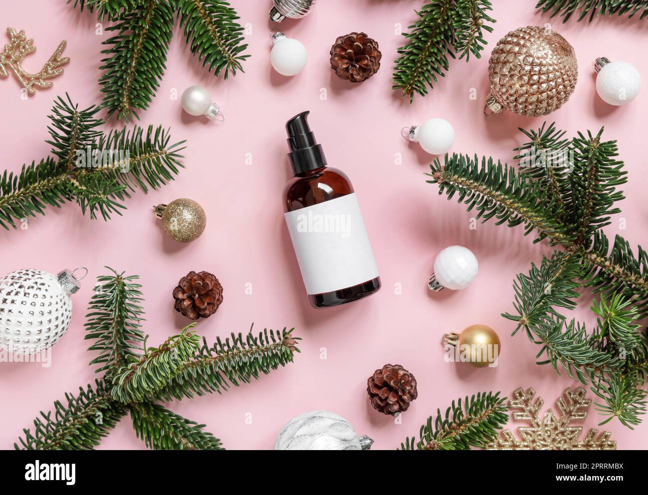Bottiglia cosmetica con pompa vicino alle decorazioni natalizie, rami di abete e coni di pino su un modello rosa Foto Stock