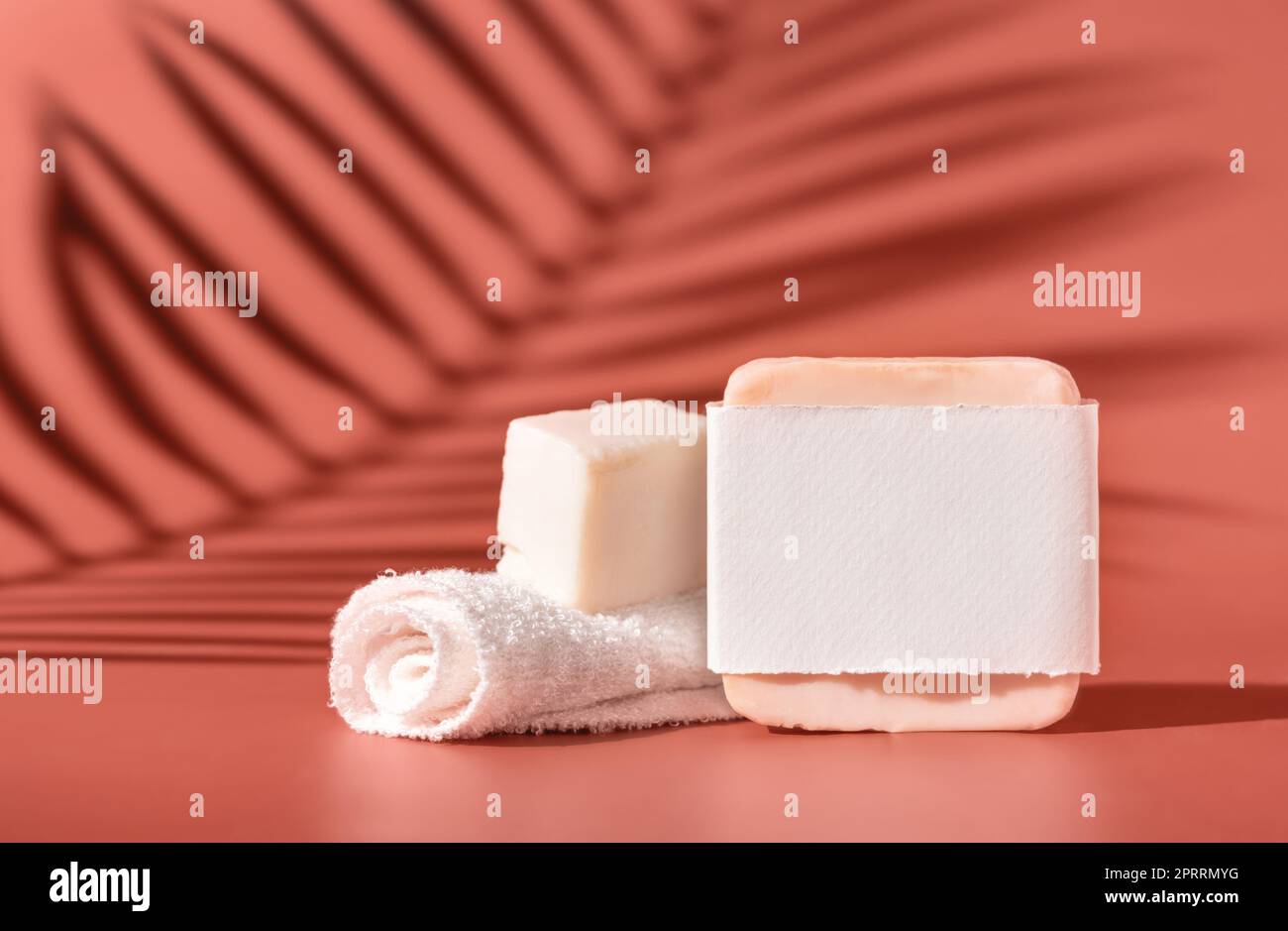 Saponette fatte a mano con etichetta vuota e piccolo asciugamano su primo piano rosa, ombre dure con foglie di palma Foto Stock