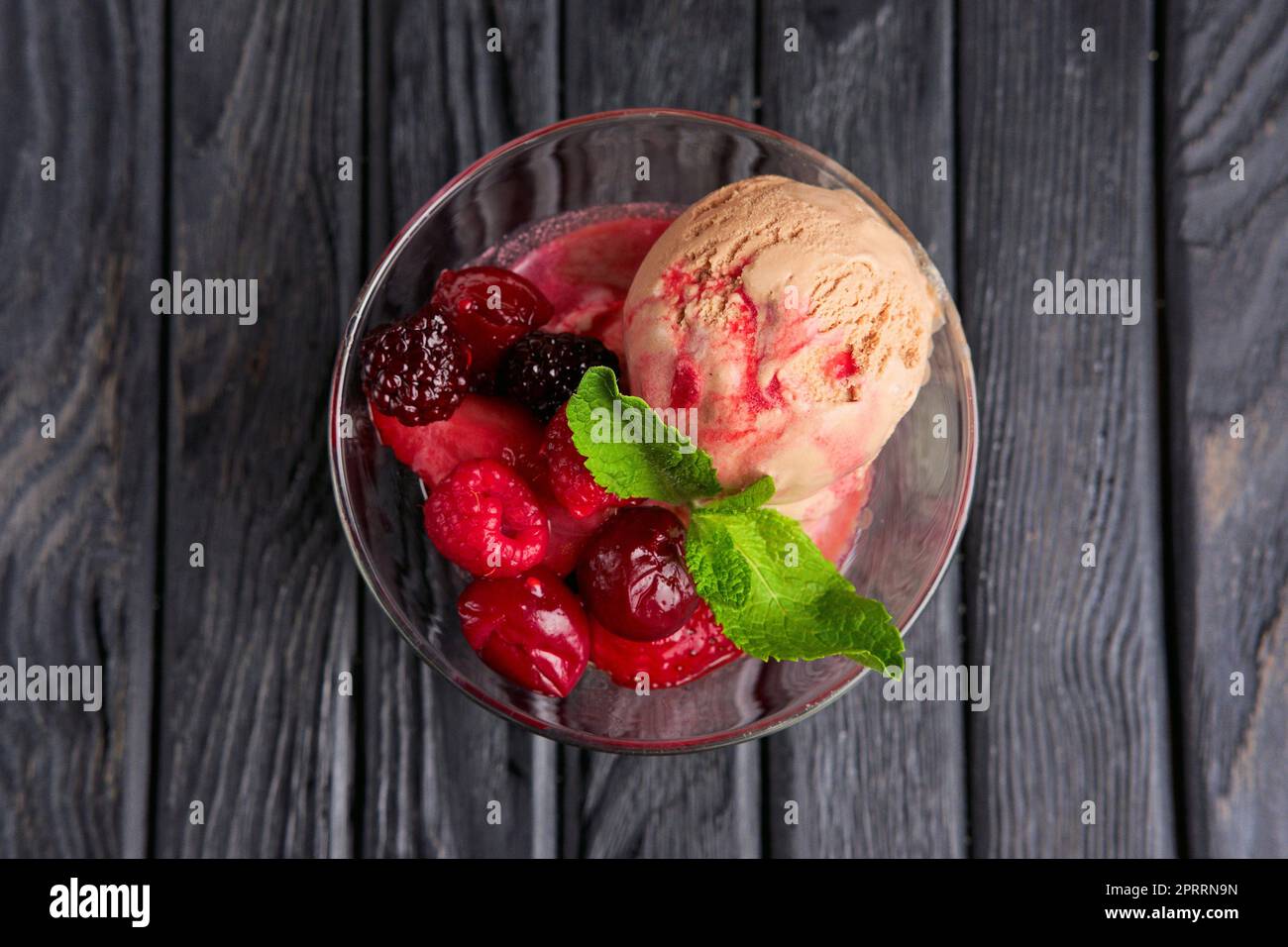 Una tazza di gelato alla ciliegia decorata con lamponi e foglie di mirtillo e menta Foto Stock