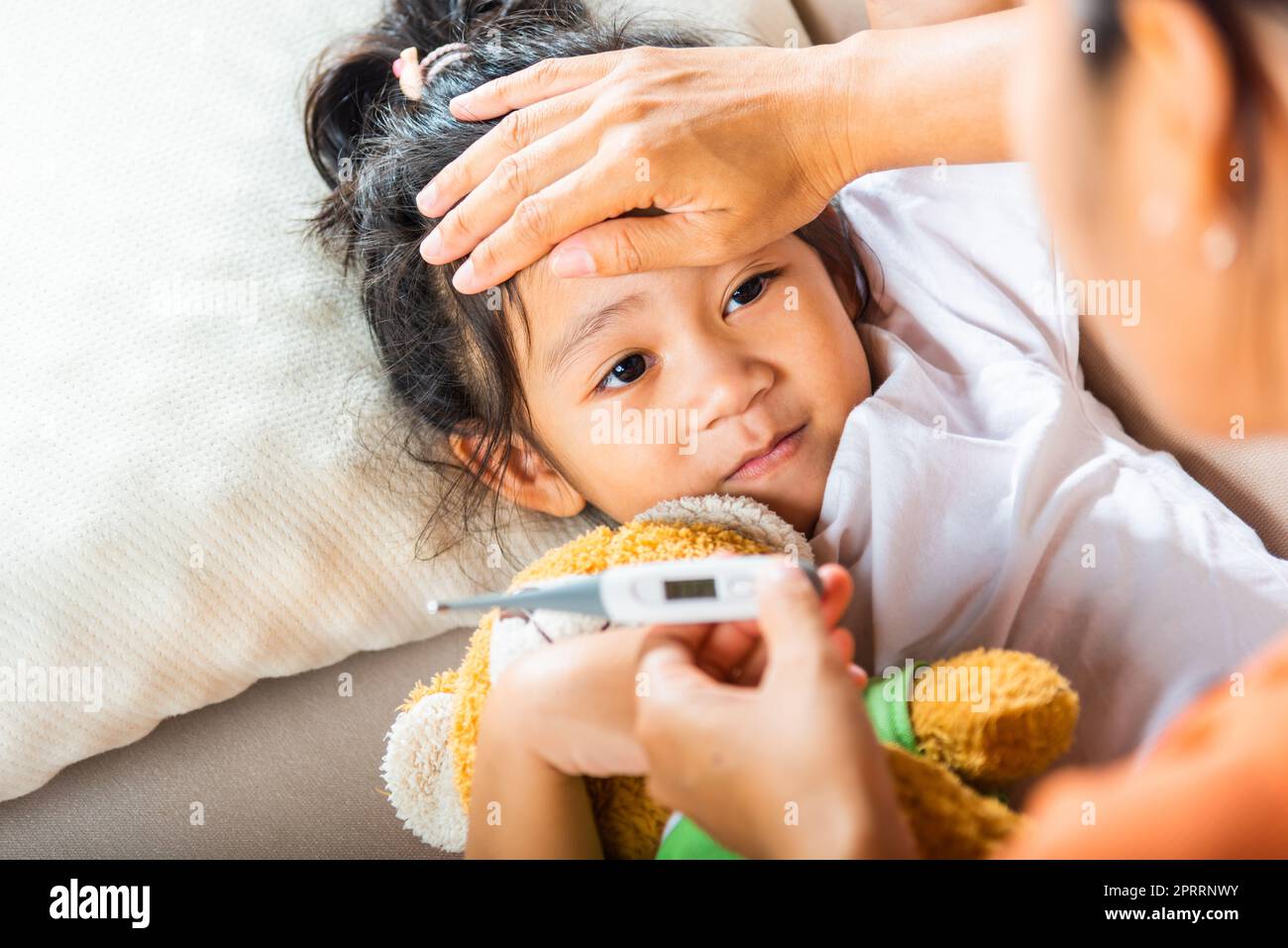 Madre genitore che controlla la temperatura di sua figlia malata con termometro digitale in bocca Foto Stock